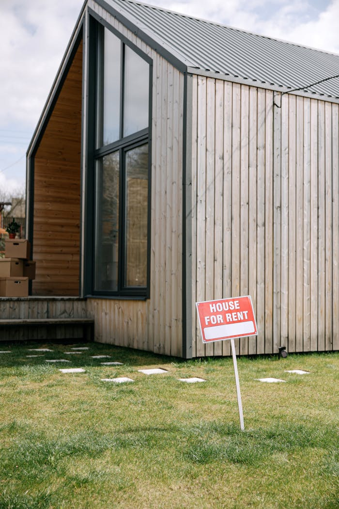 A contemporary wooden house with a prominent 'House for Rent' sign on the lawn.